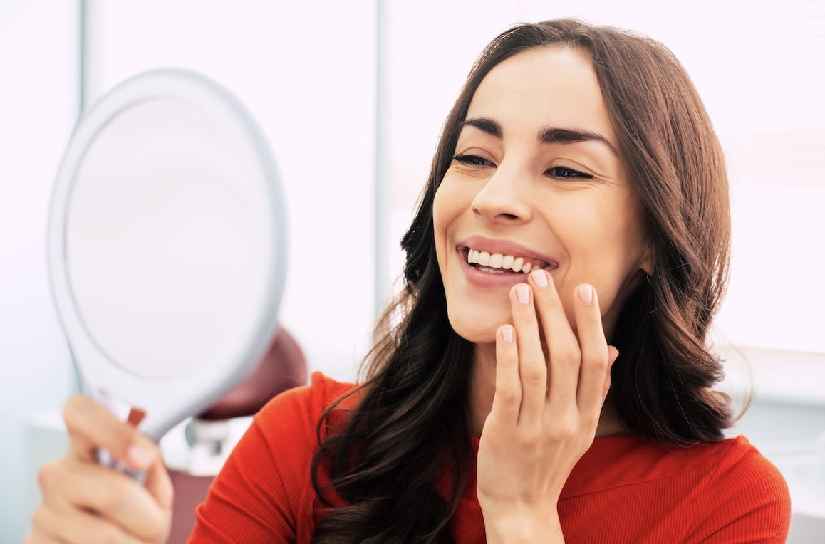 Patient-smiling-dental-implant Woman smiling with handheld mirror
